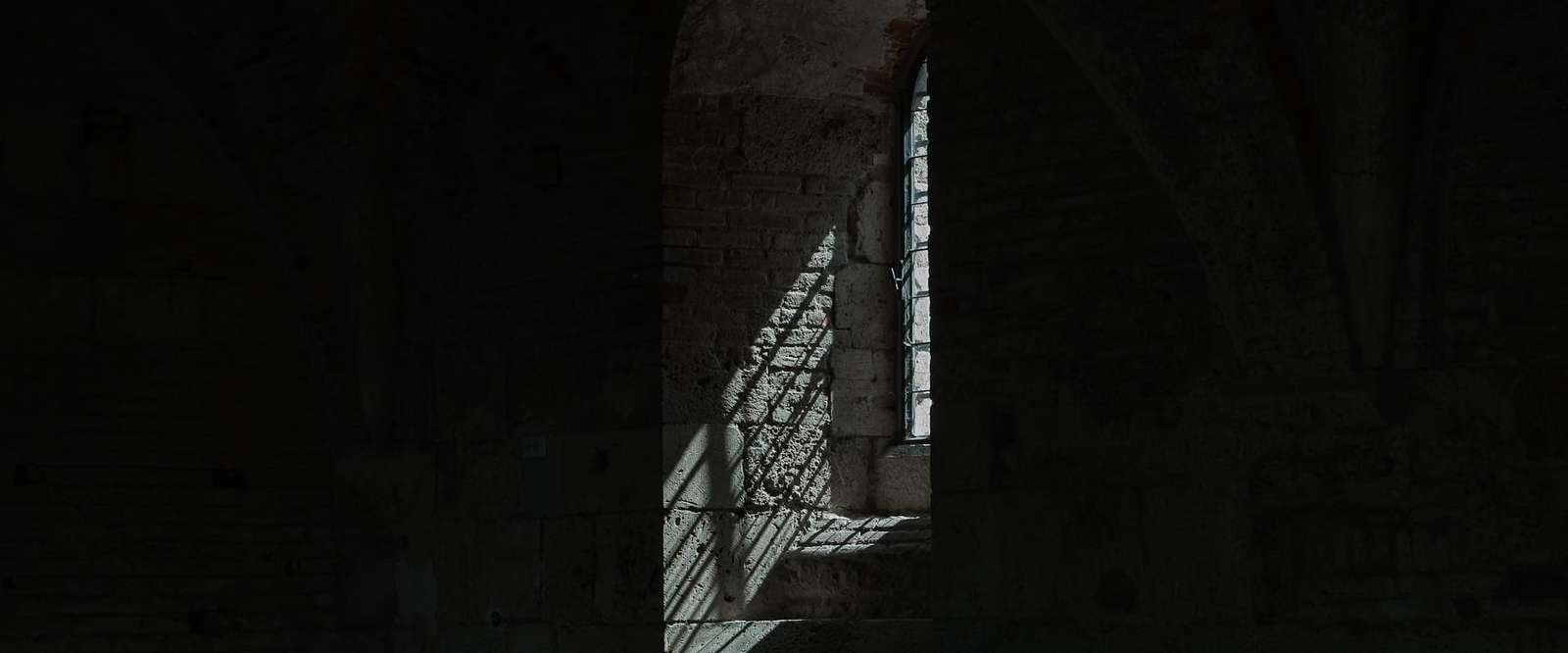 Sunlight falling through a narrow arched window onto old stone